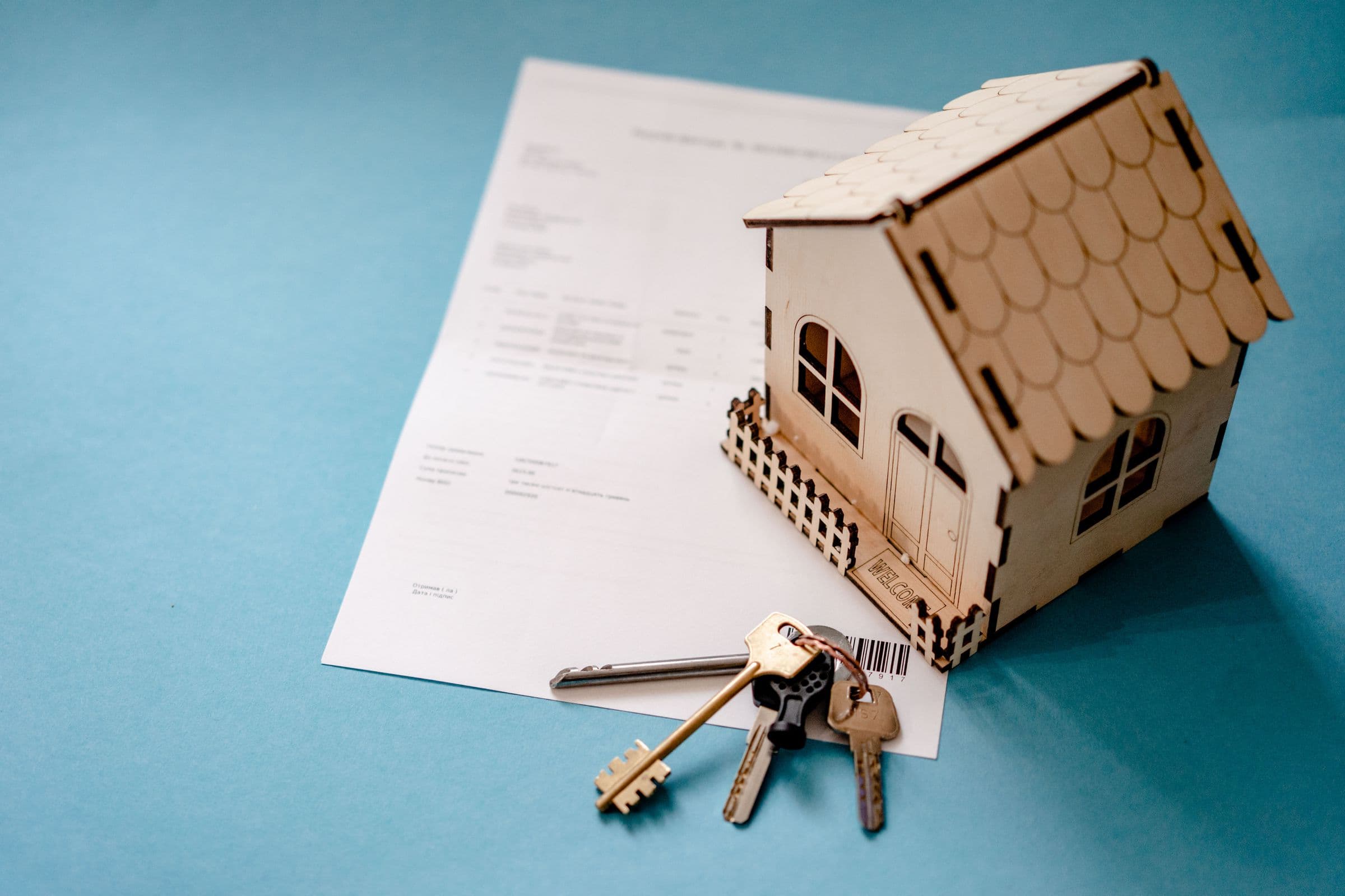 Una casita de madera en miniatura y un juego de llaves sobre un contrato firmado