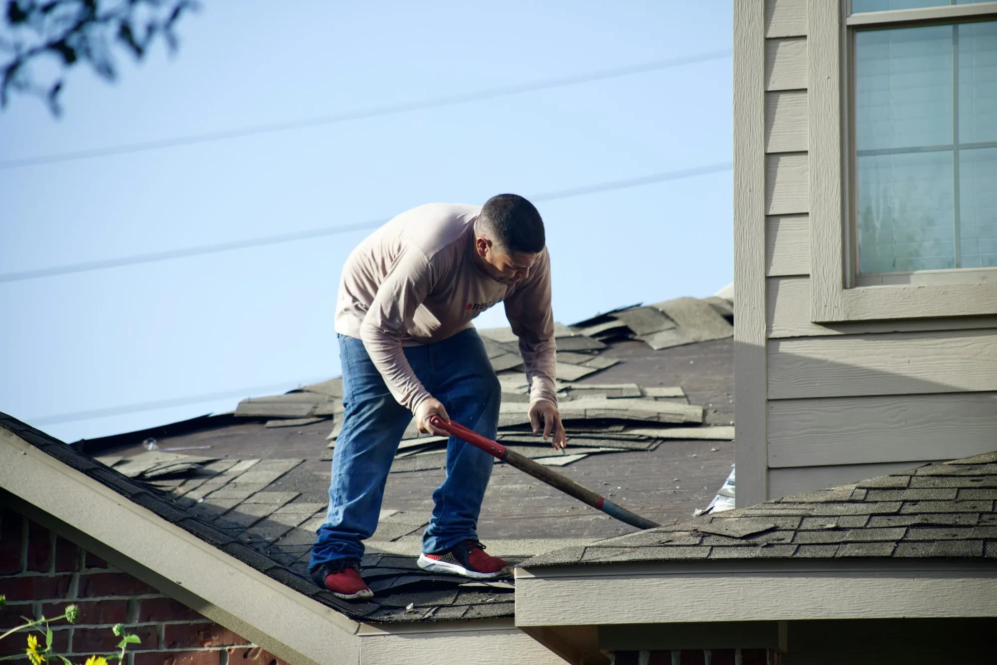 A worker stripping curled, aged shingles from a house roof
